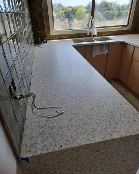 Speckled stone L-shaped kitchen benchtop with a hose across it and a mirrored splashback behind