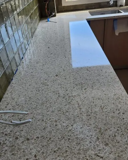 Speckled stone kitchen benchtop after polishing, clean, mirrored splashback reflecting trees outside