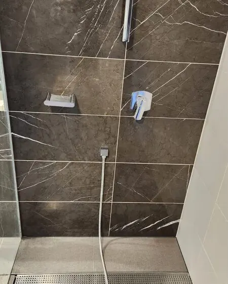 Shower with dark grey marble wall tiles, a chrome mixer and a dull surface film