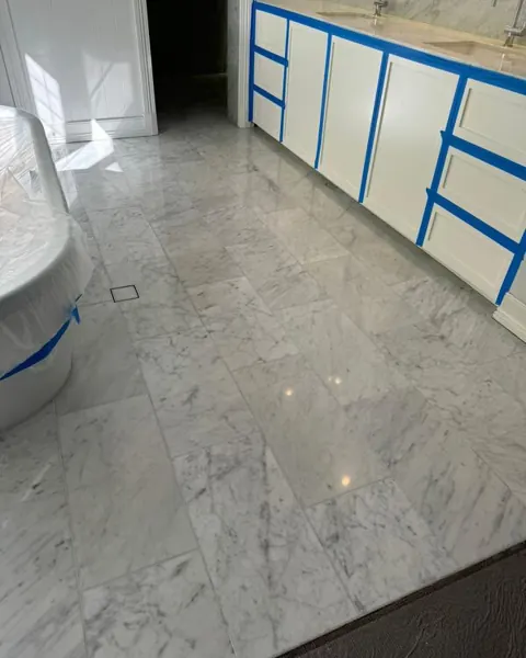 White marble bathroom floor after polishing, cabinets still masked, freestanding bath on the left