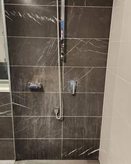 Shower with dark grey marble wall tiles after cleaning and sealing, veining clear, chrome fittings
