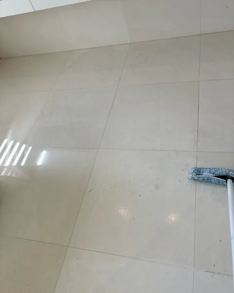 Cream marble bathroom floor mid-polish with a squeegee, light from a window on the right