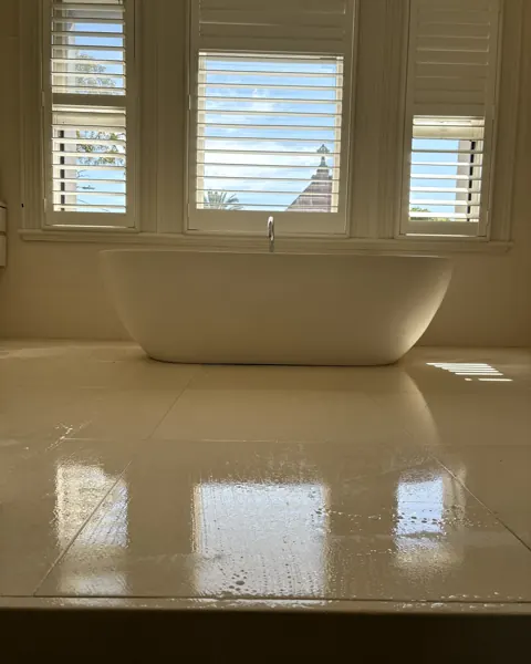 Cream marble bathroom floor polished to a reflection, freestanding bath and plantation shutters behind
