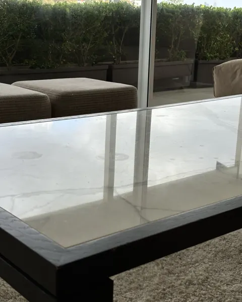 White marble coffee table top on a black frame, surface flat and matte, outdoor seating visible through the window