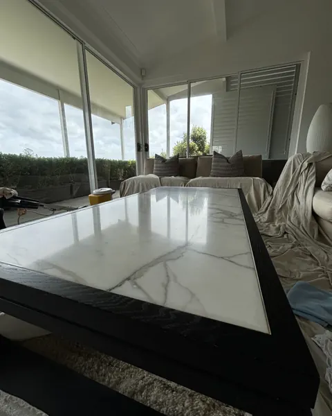 White marble coffee table top polished to a gloss, reflecting the window and garden