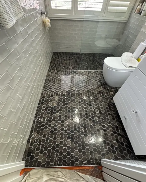 Bathroom with a black hexagon mosaic floor, drop sheets down, toilet and vanity along the wall