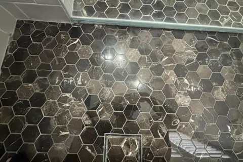 Close view of a black hexagon mosaic floor with dull, hazy patches and uneven shine