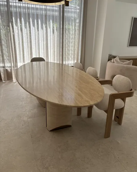 Oval travertine dining table with curved timber chairs in a living room with sheer curtains