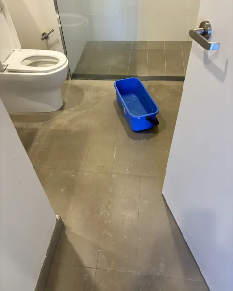 Grey stone bathroom floor mid-clean with a blue bucket beside the toilet