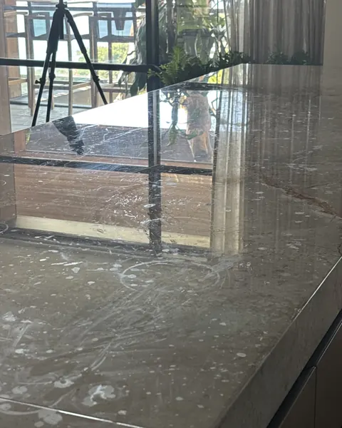 Close view of a grey marble island top reflecting a black window frame and the room beyond