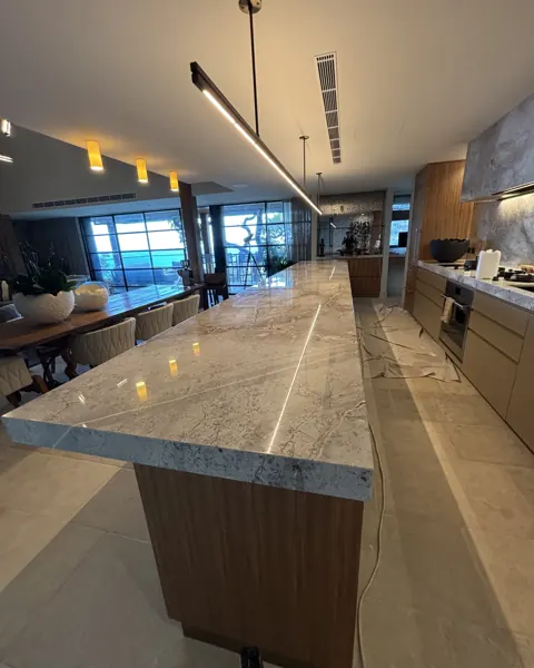Long grey marble kitchen island in a timber kitchen, polished to a reflection, pendant light above