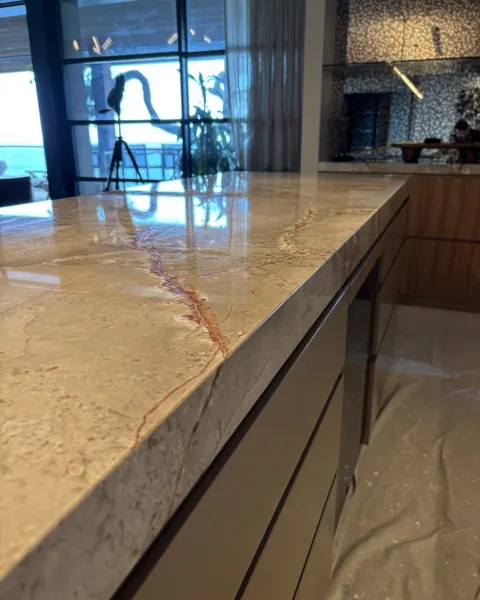 Polished tan marble benchtop reflecting a window frame, the surface like a mirror
