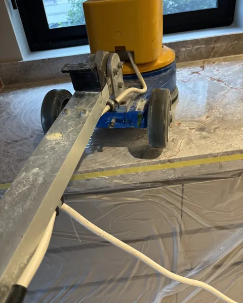 Polishing machine sitting on a tan marble benchtop with masking tape along the splashback and a window behind