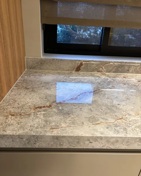 Close view of a tan marble benchtop with a small rectangular test patch polished to a higher gloss than the surrounding stone