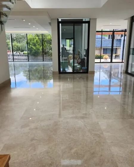 Double-height entry hall with a polished cream marble floor reflecting the glass doors and stair